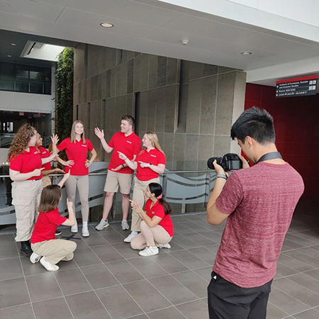 A photographer taking a photo of a group of students all wearing the same red and beige outfit.