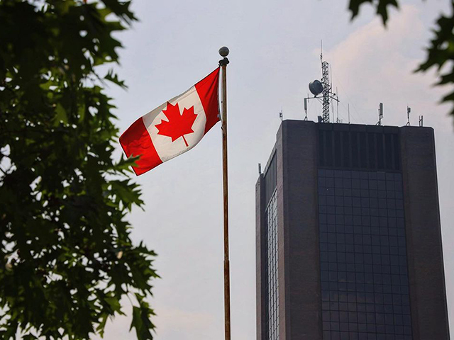 A large office building flanked by a Canadian flag blowing in the wind.