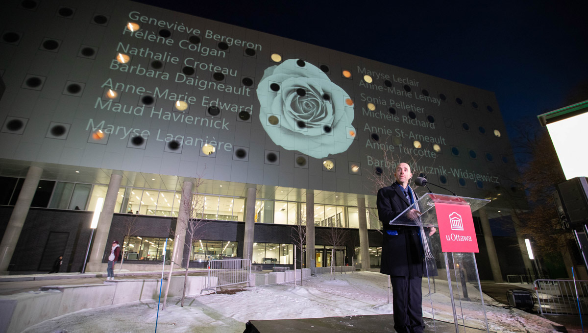 President Benoit-Antoine Bacon speaks at a podium at uOttawa during a vigil commemorating victims of the Montreal Massacre.