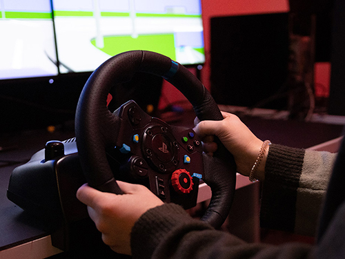 A pair of hands grasping the steering wheel of a driving simulator.