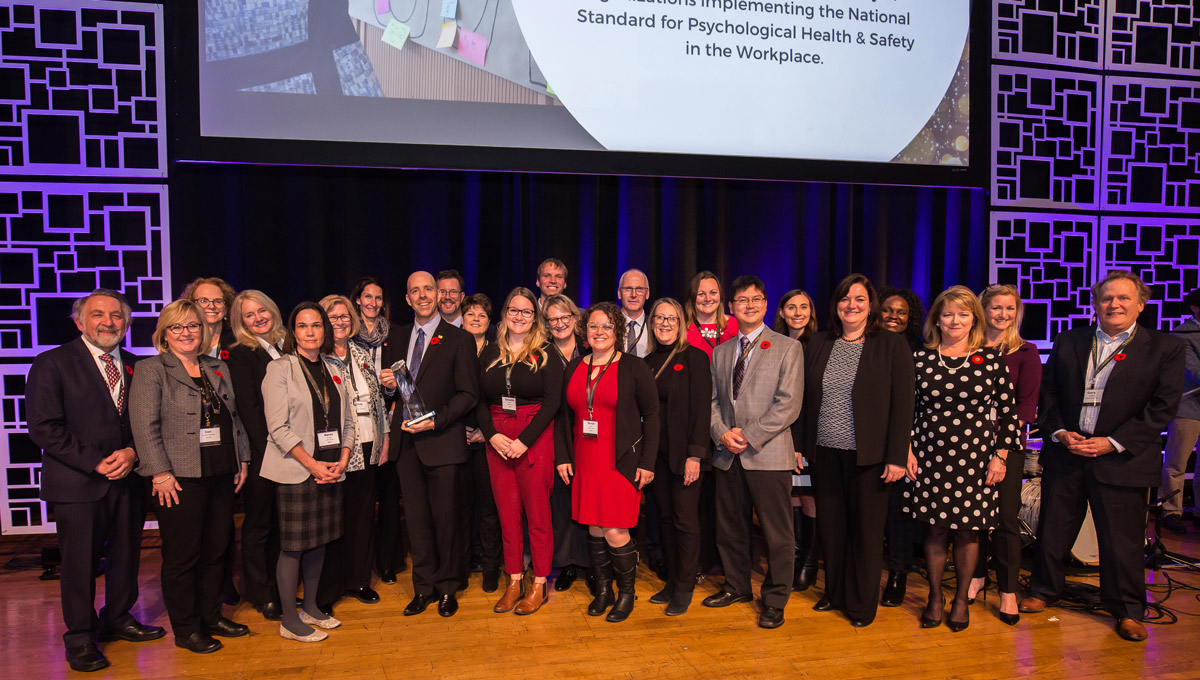 A large group of Carleton faculty and staff members stand together on stage during the Excellence Canada awards ceremony.