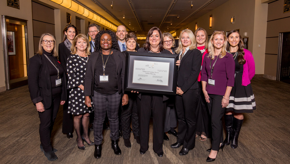 A large group of Carleton faculty and staff members stand together in a hallway during the Excellence Canada awards ceremony.