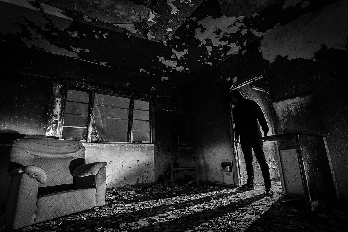 A dark, decaying room with a faceless silhouette in the doorway — symbolic of Indigenous stereotypes, erasure, and horror in modern storytelling.