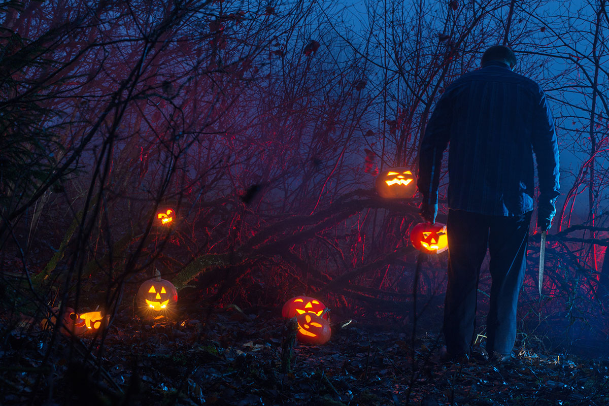 Man holding a pumpkin and knife in a dark forest surrounded by glowing jack-o’-lanterns — representing Indigenous stereotypes and horror imagery in modern storytelling.