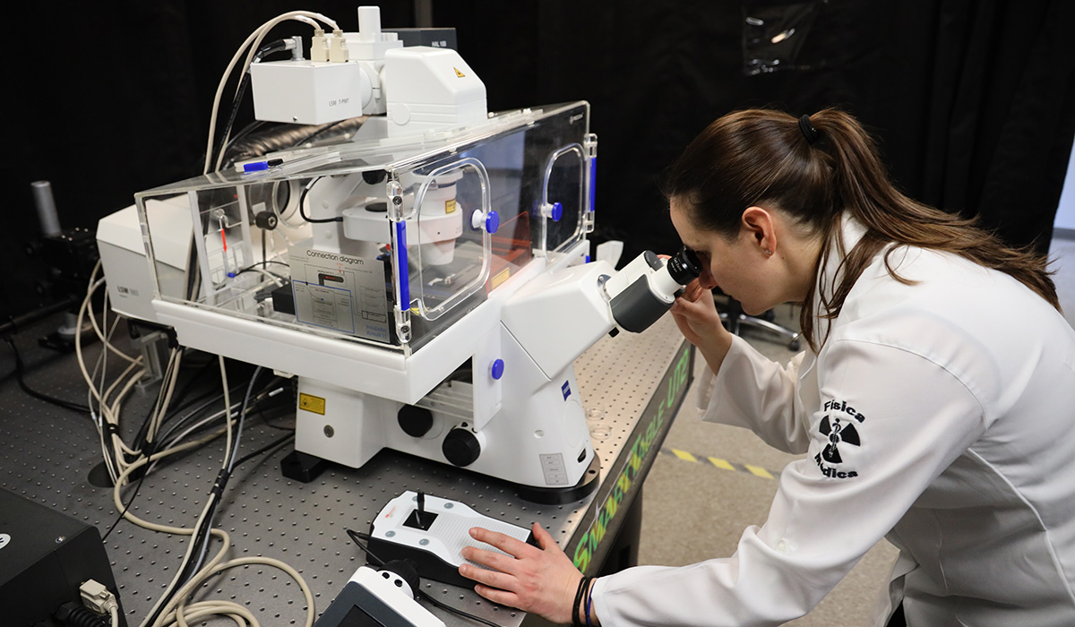 A woman in a lab coat looks into a high-powered microscope.