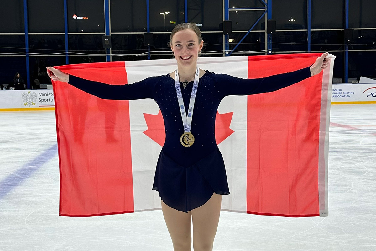 A figure skating champion poses with her gold medal while holding up a Canadian flag.