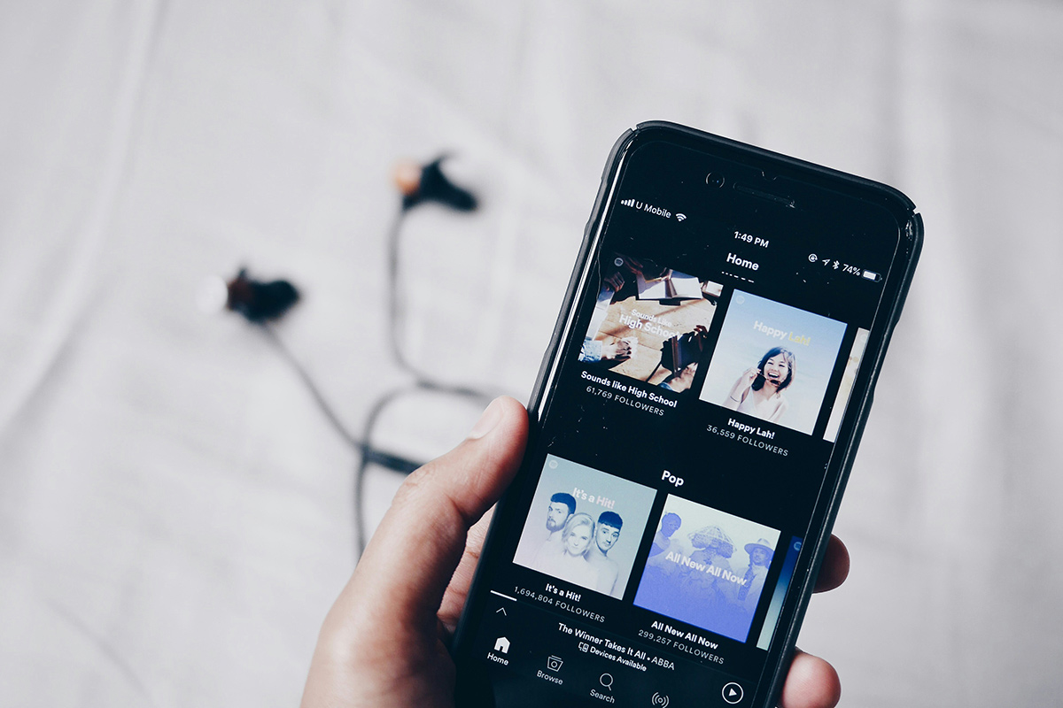 A hand holding a mobile phone with the Spotify app open.