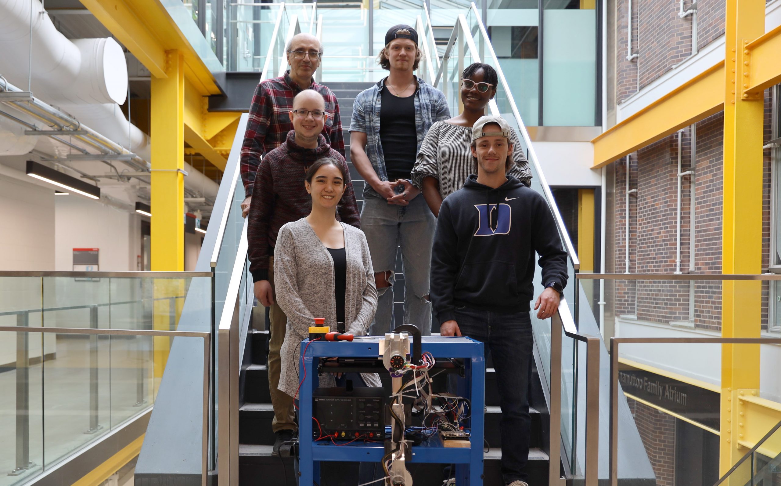 Six individuals stand on a staircase in front of a robot leg