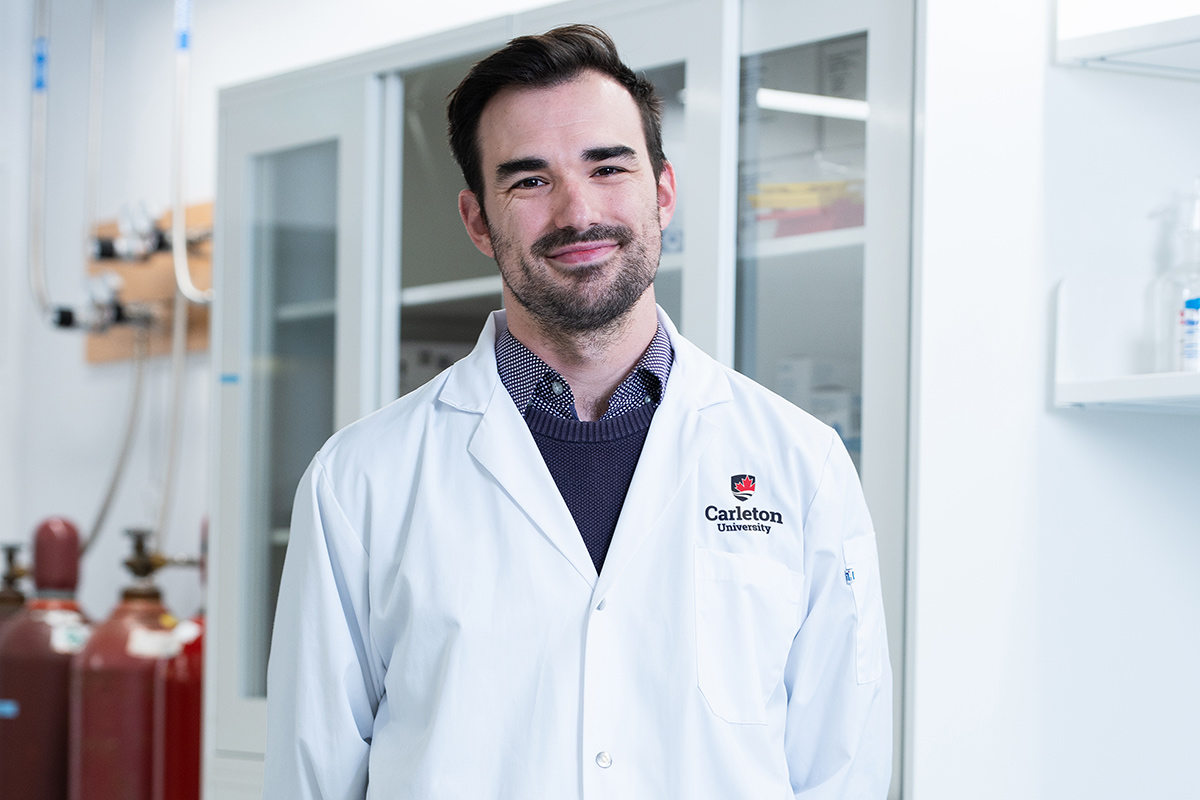 A man wearing lab coat poses for a photo inside a lab.