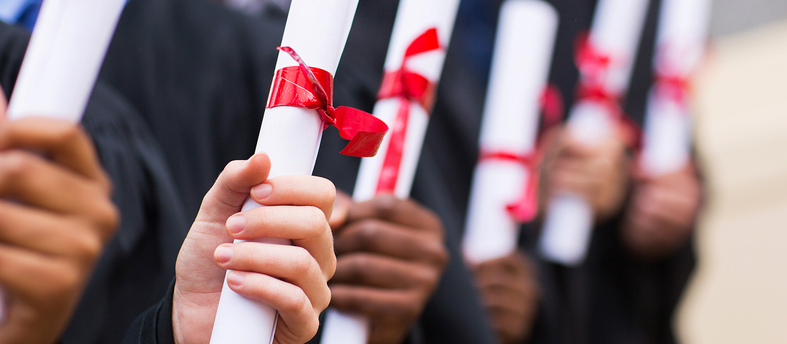 A row of students holding their degrees. Only hands and degrees are visible.