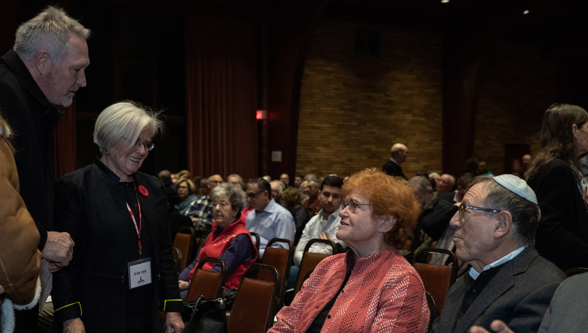 Several standing audience members speak to Deborah Lipstadt, who is seated, after she has finished her lecture.