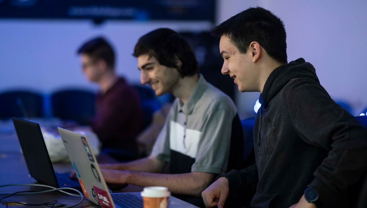 Two competitors type on a laptop while laughing during the iHack event.