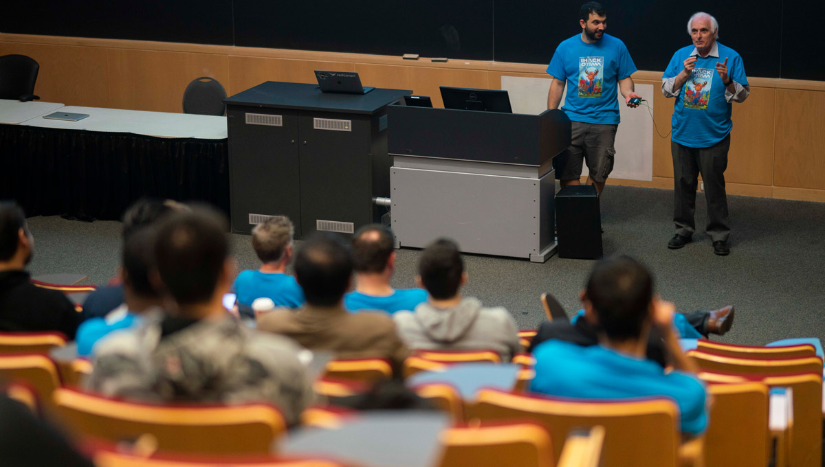 Attendees listen as a presenter speaks at the podium during the iHack event.