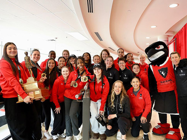 A sports team poses for a group photo with a team mascot and the coach.