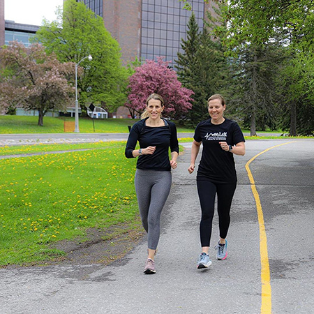 Two women running towards the camera down a bike path.