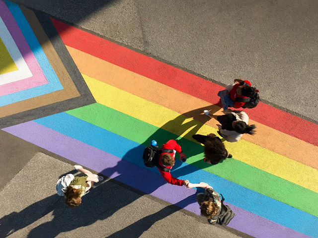 A birds eye view of people crossing a pride flag themed crosswalk.