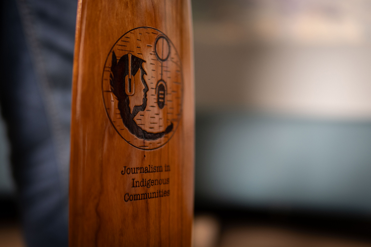 An oar with a design carved into the wood along with the words 'Journalism in Indigenous Communities.'