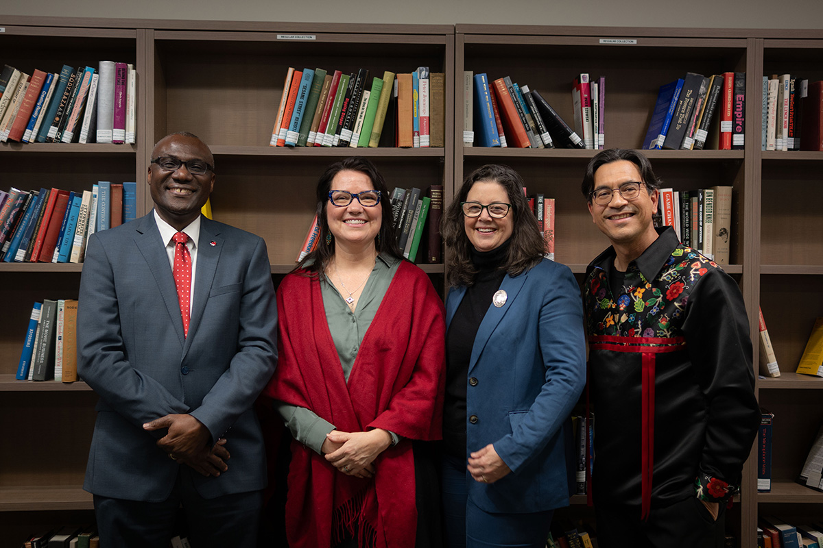 Four people posing for a photo in front of a bookshelf.