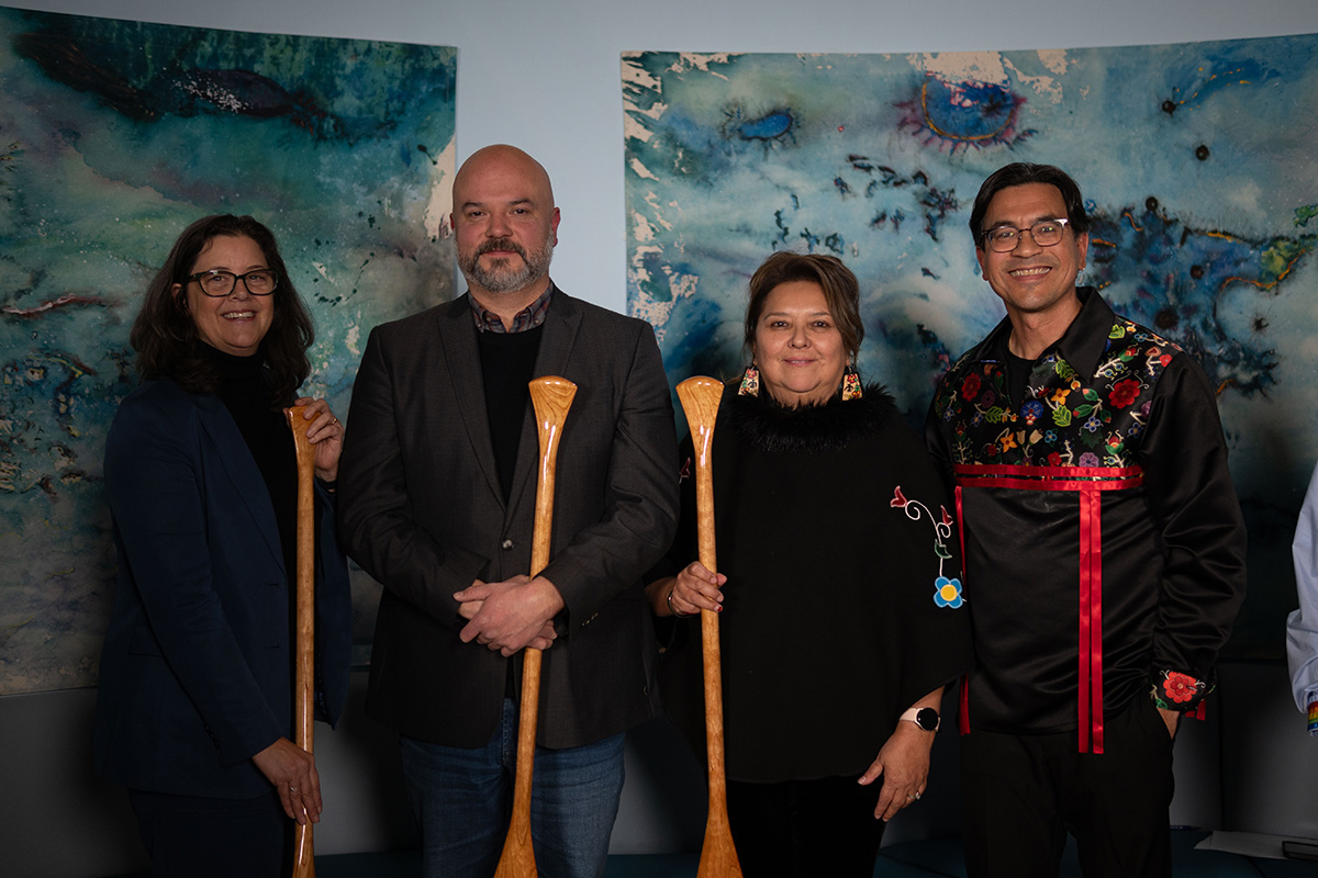 Four people posing for a photo while holding wooden oars.