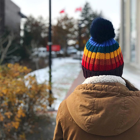 A view from behind of a someone on the Carleton campus wearing a colourful toque