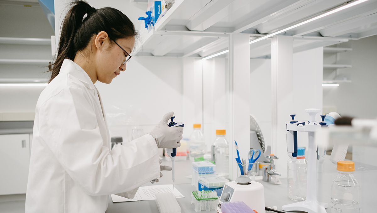 A scientist in a white lab coat with white gloves uses a pipette while investigating food fraud.