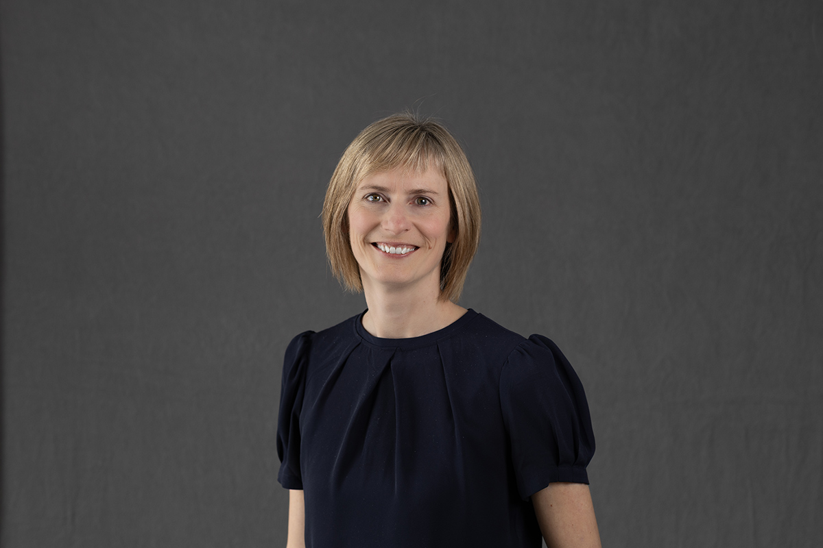 A woman with short hair and a dark shirt poses for a professional photo with a dark backdrop behind her, for a story about them being named to the 2025 Dorothy Killam Fellowships.