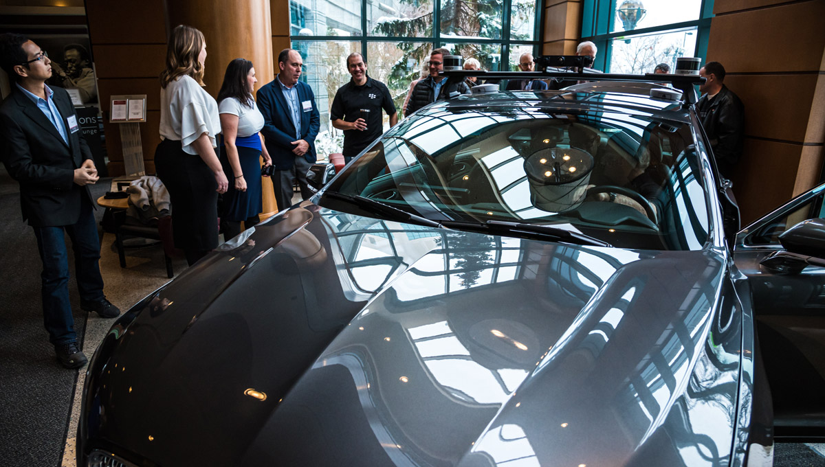 Luncheon goers gather around and inspect a connected and autonomous vehicle in a hotel lobby.