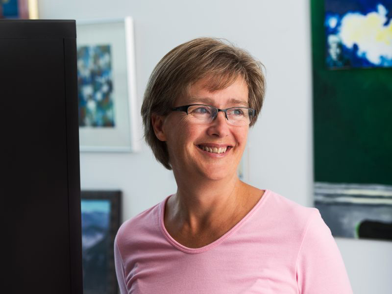 A woman with short hair in a pink shirt smiles while looking away from the camera.