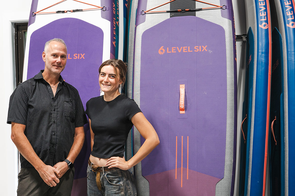 A man and woman pose for a photo in front of surfboards designed by Level Six