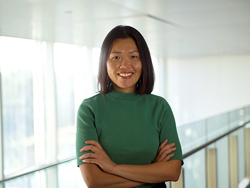 A woman in a green shirt with her arms crossed smiles for the camera