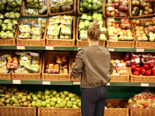 middle aged woman standing in front of produce inside a groccery store