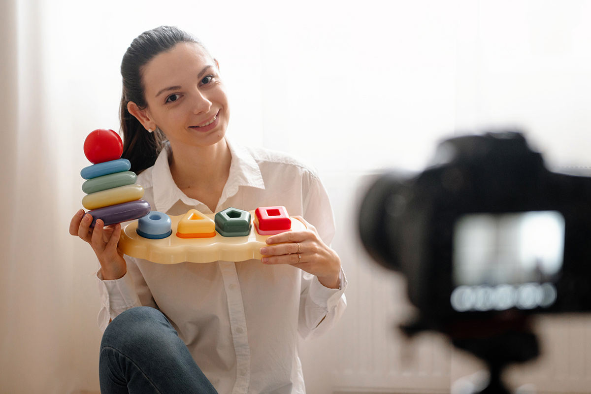 A young woman films her self holding up baby toys.