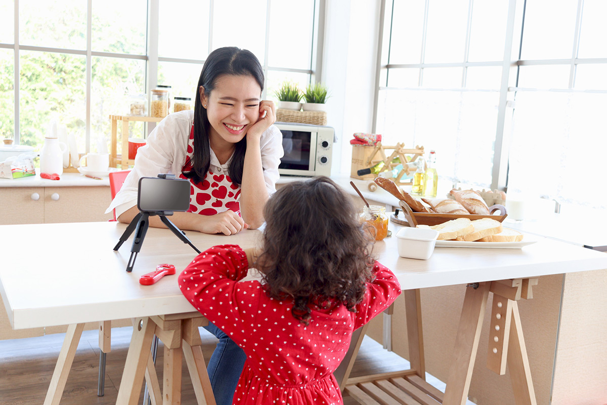 A smiling mother interacts with a child in a kitchen.