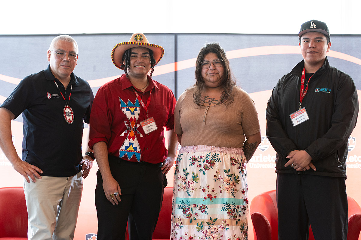 Four people posing for a group photo in front of three 3 chairs.