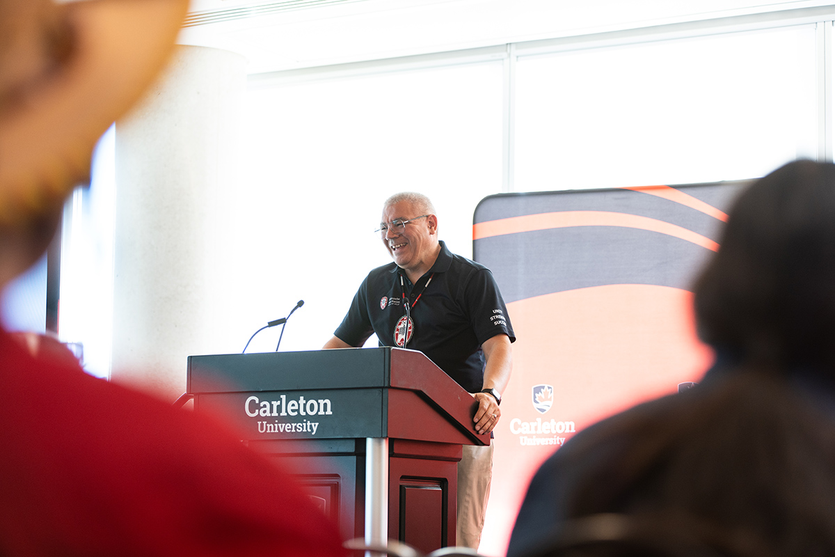 A man wearing glasses speaks to a crowd from a podium.