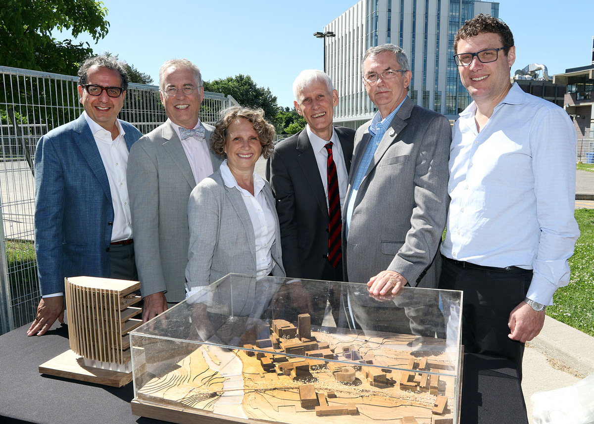 Stakeholders stand around a to-scale model of the new Sprott building on a sunny day.