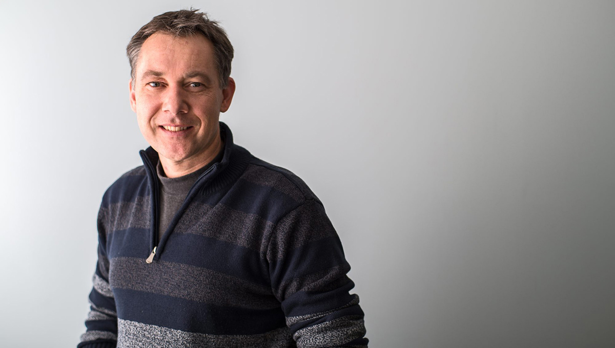 A man with a stripped zip up sweater poses for a professional photo.