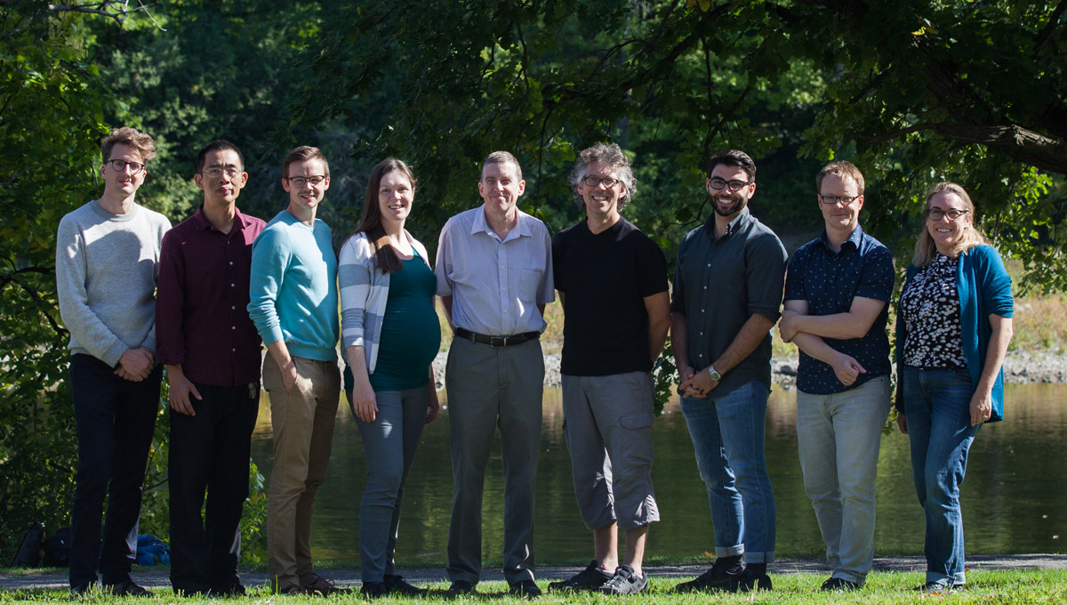 The Ottawa Medical Physics Institute stands together on a sunny day with the Rideau River in the background.