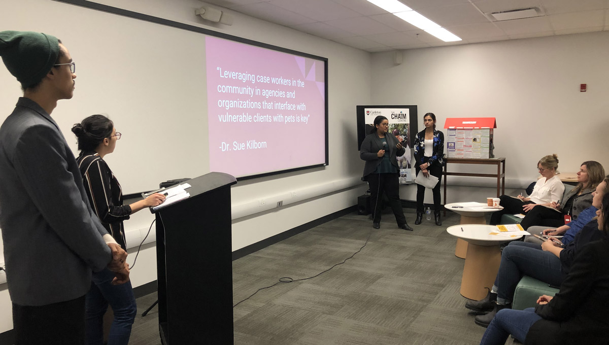 A projector displays a powrerpoint presentation while students speak to an audience in a conference room during the One Health Challenge.