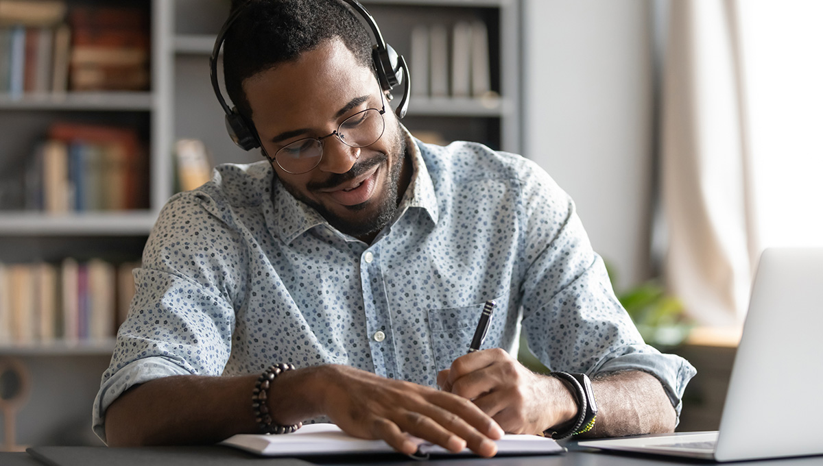 A student wearing a headset and taking notes