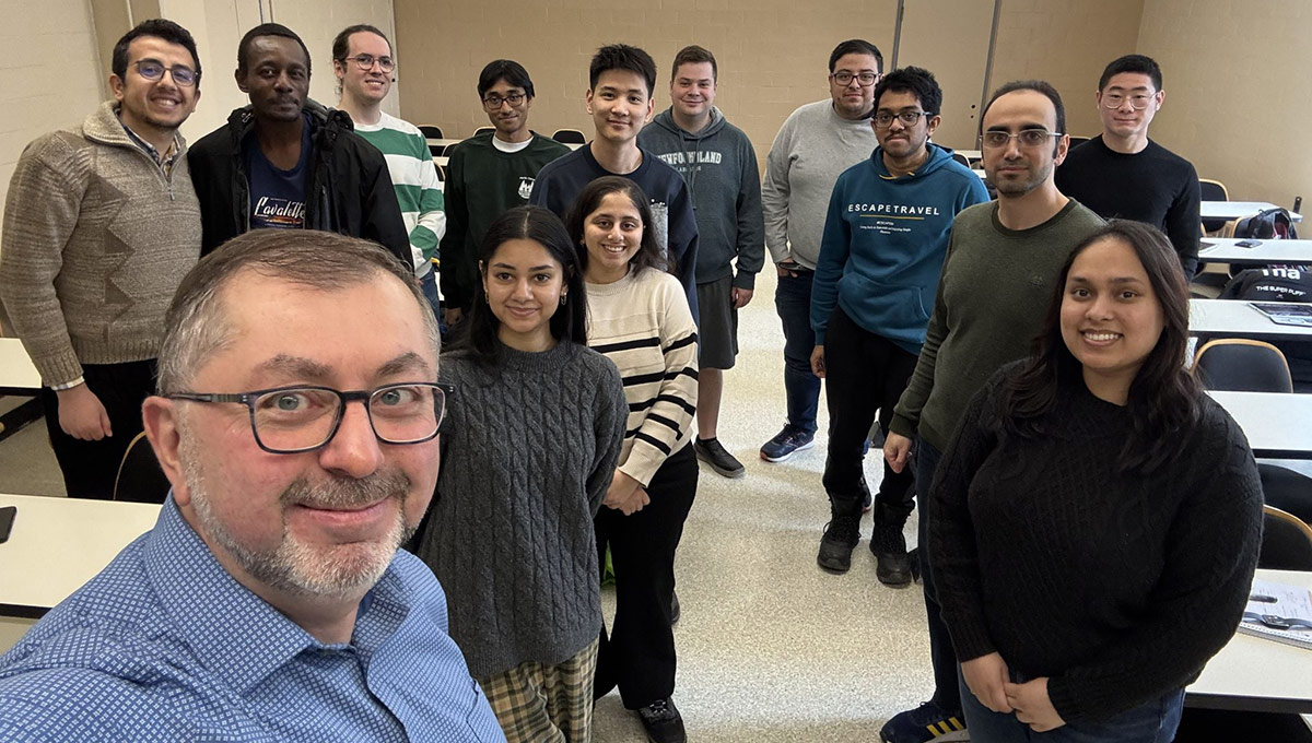 A man holds up his device to take a selfie with a large group of people behind him, a team researching Non-Terrestrial Networks.