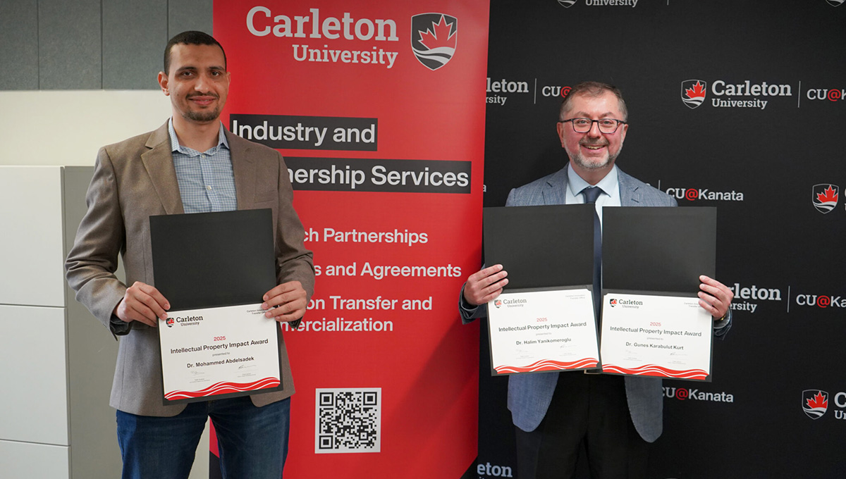 Two professionally dressed people holding up certificates in front of a promotional banner.