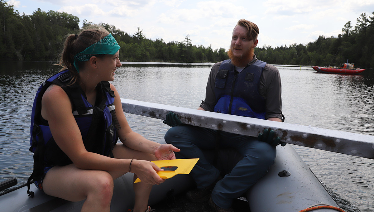 Two members of a Anthropocene research team sit on a boat in a lake with a large piece of freeze core on one of their laps.