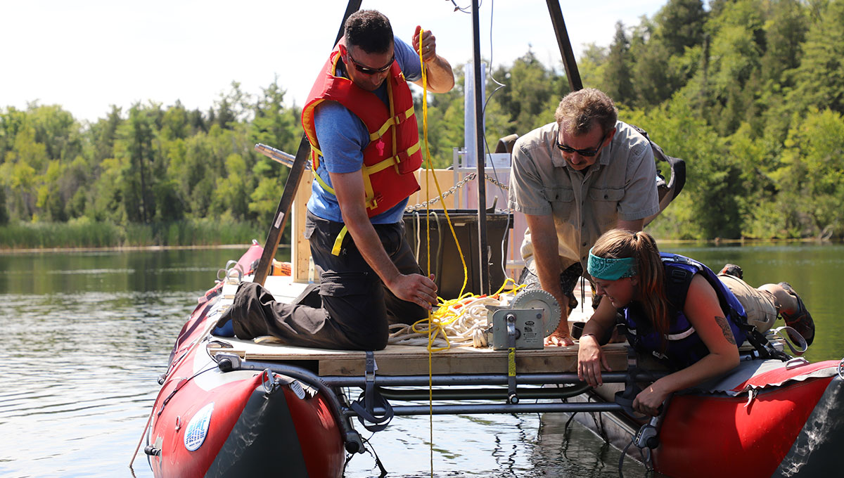 Researchers leaning off a boat with equipment to collect data