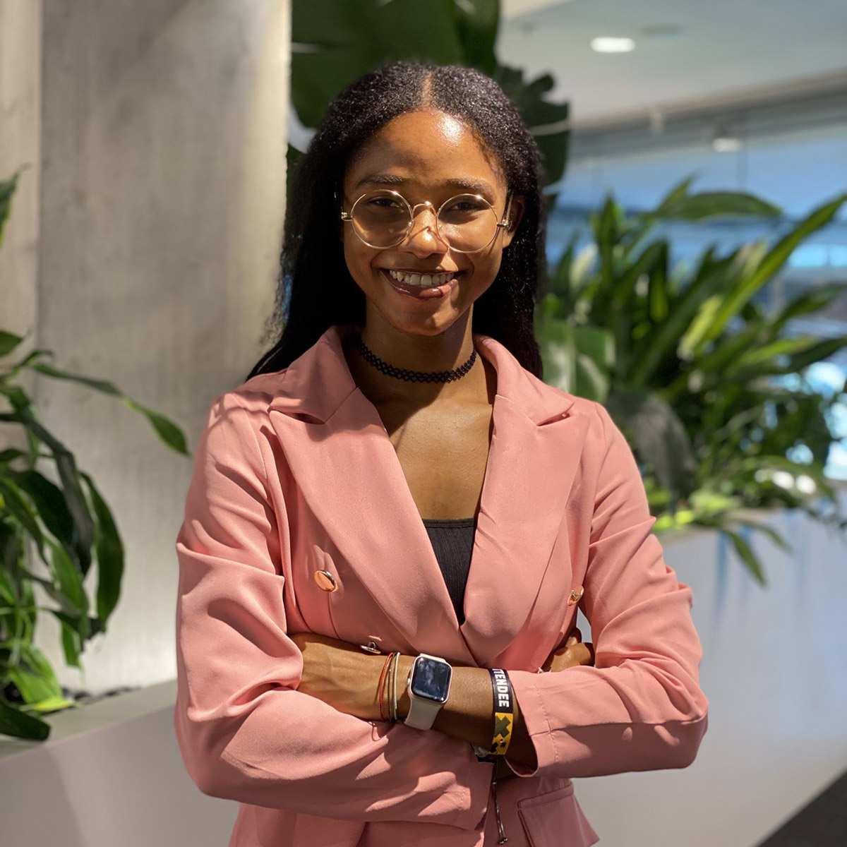 A woman studying health and AI is wearing a pink sweater while posing for a photo with her arms crossed.