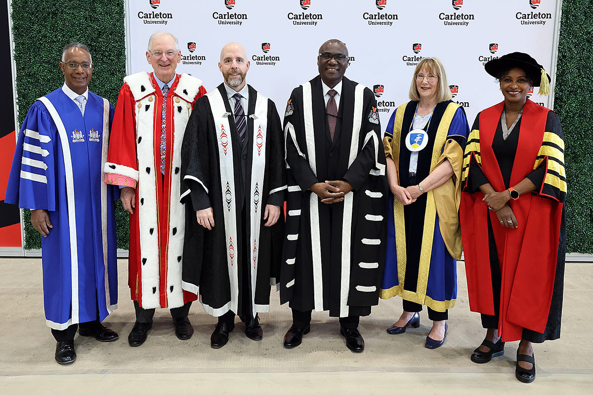 Six people wearing academic regalia pose for a group photo.
