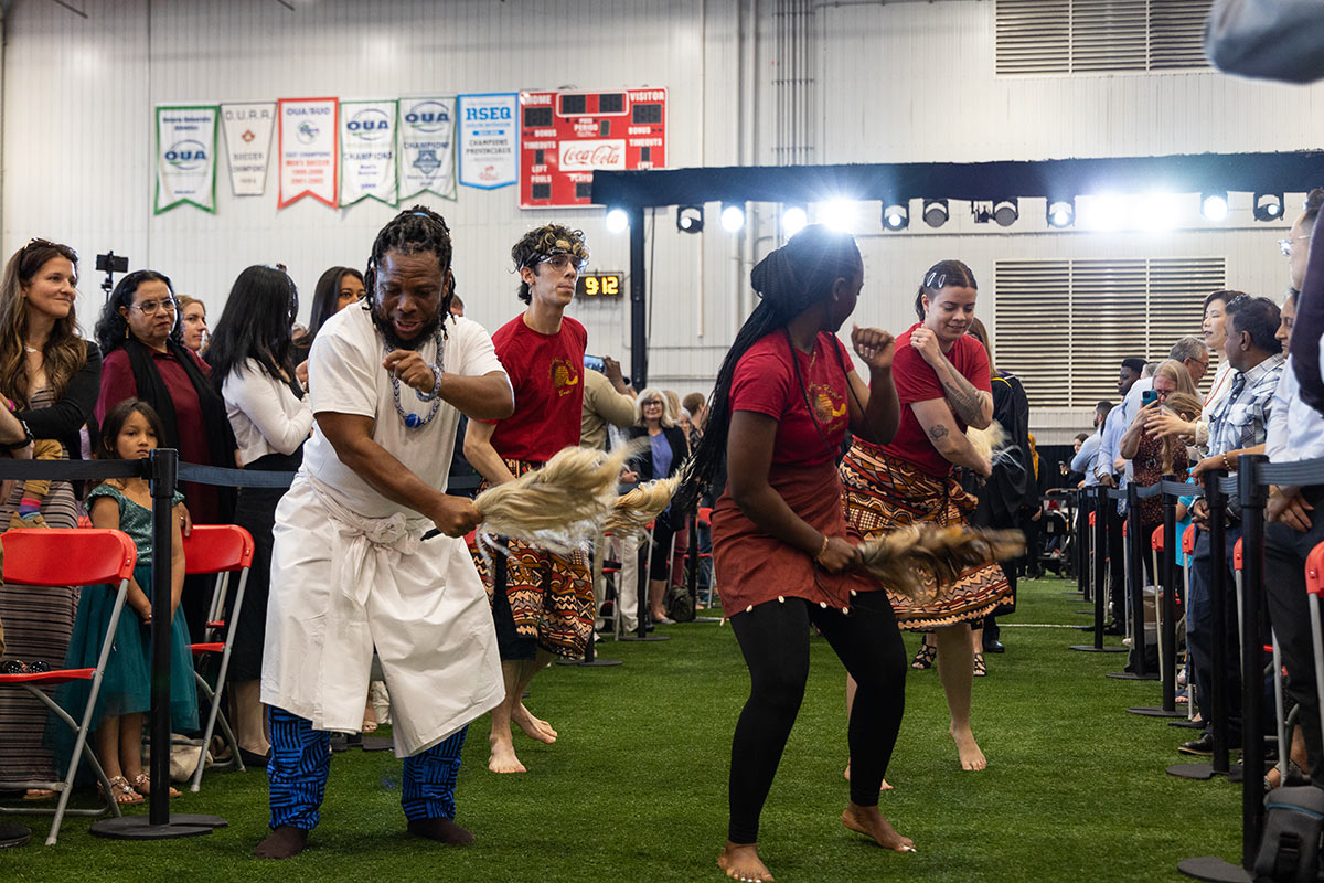 Four people performing a traditional dance as an audience looks on.