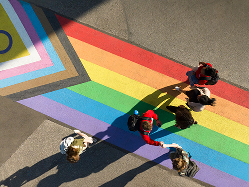 An aerial view of people walking across a rainbow painted crosswalk.