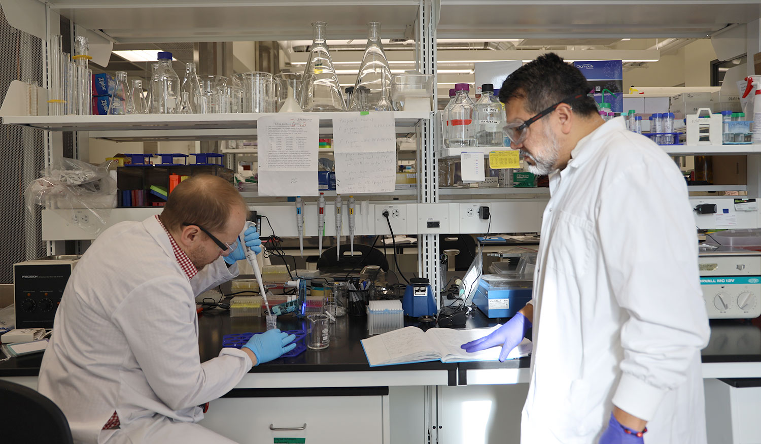 A scientist observes another scientist working with a sample.