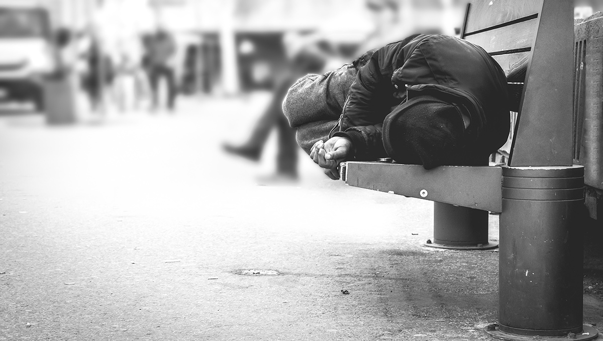 A homeless person sleeps on a sidewalk